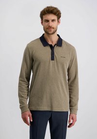 Beige Langarm-Polohemd mit strukturiertem Muster, dunkelblauem Kragen, Dreiknopfleiste und gesticktem Logo auf der linken Brust; kombiniert mit dunklen Hosen.