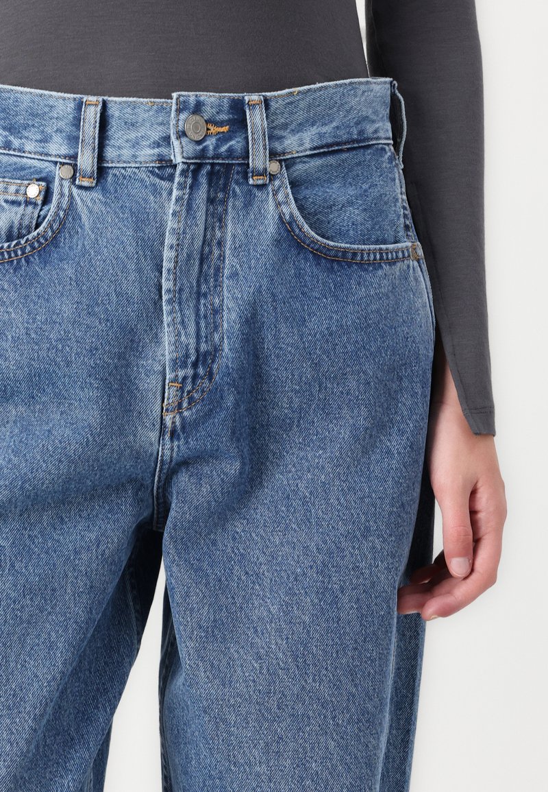 Blaue Denim-Jeans mit hoher Taille, Fünf-Taschen-Design und kontrastierenden Nähten. Mit vorderem Knopfverschluss und leichter Used-Optik.