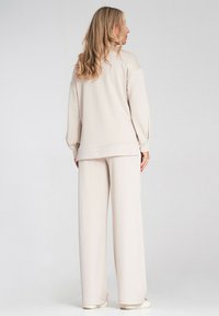 Beżowy dres o luźnym kroju. Bluza ma obniżone ramiona, a spodnie o szerokich nogawkach charakteryzują się gładką teksturą i elastycznym pasem.