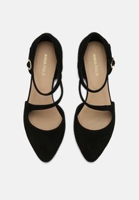 Svarta mocka högklackade skor med spetsiga tår, prydda med flera korsade remmar och en liten spänneaccent. Slät inre foder.