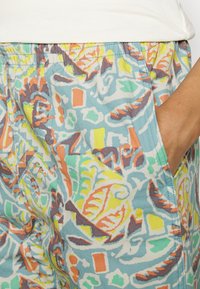 Colorful patterned fabric shorts featuring a mix of blue, orange, yellow, and green geometric and leaf designs, with an elastic waistband and side pockets.