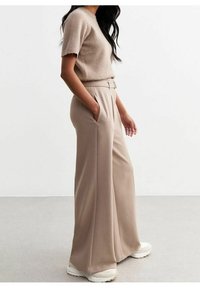 Beige kortärmad tröja i mjukt material, kombinerad med högmidjade, vida byxor i en matchande ljusbeige färg.