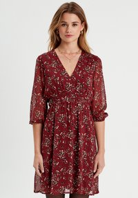 Robe fleurie bordeaux en tissu léger, avec un col en V, des manches trois-quarts et une taille élastique. Comprend une jupe évasée.