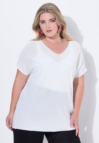 Blusa bianca leggera con scollo a V e maniche corte, caratterizzata da un sottile design gradient. Tessuto morbido, vestibilità comoda. Pantaloni neri.