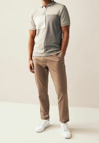 Polo gris clair zippé avec un panneau blanc, associé à un pantalon beige et des baskets blanches. Texture lisse et coupe classique.