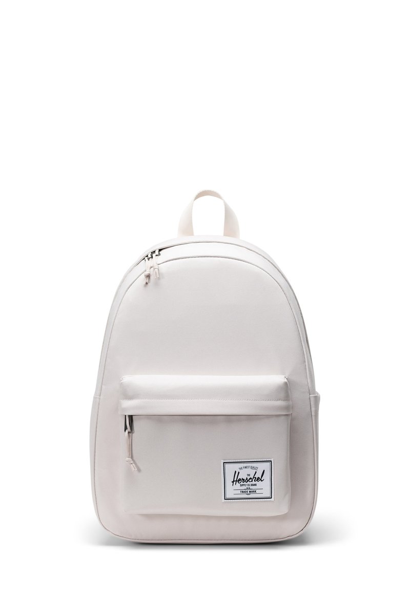 Sac à dos beige clair en tissu résistant, avec une forme arrondie, une poche zippée à l'avant et une poignée de transport en haut. Patch avec le logo Herschel visible.