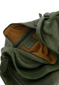 Groene leren handtas met gewoven textuur, bruine stofvoering, ritszak en een merklabel aan de binnenkant. Zacht, duurzaam materiaal.