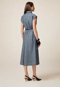 Robe en denim à manches courtes, coupée au genou, avec une taille ceinturée et une texture subtile. Portée avec des escarpins noirs à brides.