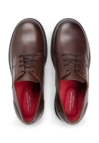 Καφέ δερμάτινα παπούτσια για φόρεμα με λείο φινίρισμα, σχεδιασμό με κορδόνια, στρογγυλεμένη μύτη, μαύρη σόλα και κόκκινη εσωτερική σόλα με το όνομα της μάρκας.