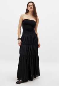 Schwarzes trägerloses Oberteil, kombiniert mit einem fließenden schwarzen, gestuften Maxirock, der einen strukturierten Stoff und einen weichen, gerafften Taillenbund aufweist.