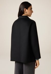 Schwarzer Wollmantel mit geradem Schnitt, minimalen Details und einem strukturierten Kragen. Verfügt über lange Ärmel und eine glatte Textur.