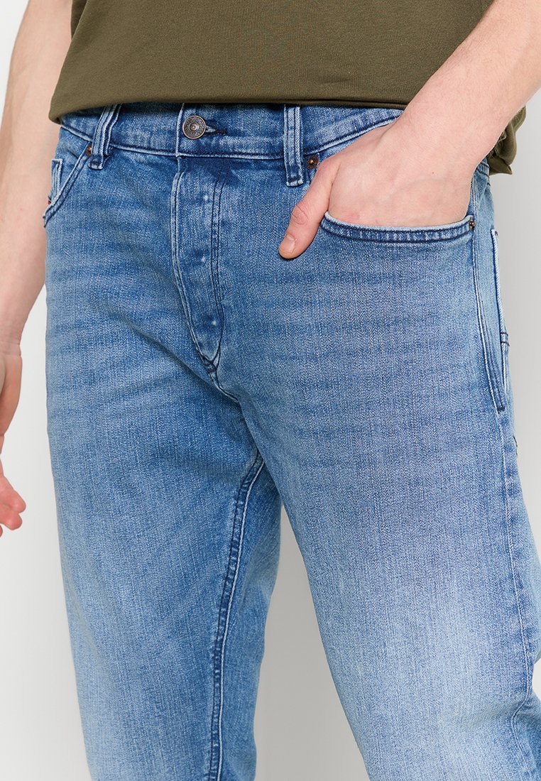 Jean en denim bleu délavé avec une coupe droite, un design à cinq poches et une fermeture à bouton à la taille. Le tissu présente une texture et un motif subtils.