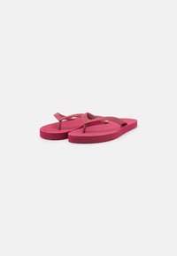 Pink flip-flops made of rubber with a flat sole, thin straps, and a textured surface. Features a circular logo on the footbed.