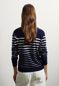 Maglione blu navy con strisce orizzontali bianche, realizzato in morbido materiale, con colletto a girocollo e maniche lunghe. Dettaglio in maglia testurizzata visibile.