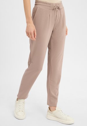 Light brown joggers with elastic waistband and drawstring. Smooth fabric, slim fit, side pockets. Paired with white sneakers.