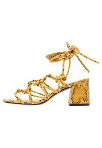 Żółte sandały na obcasie w wężowy wzór z wiązanymi paskami, otwartym noskiem, wzorzystym blokowym obcasem i wiązaniem wokół kostki.