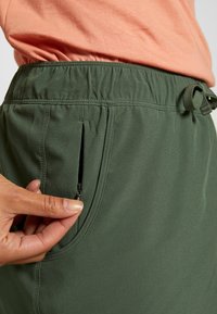 Pantalones cortos verdes hechos de una tela suave y ligera con una cintura elástica y un pequeño bolsillo con cremallera en el lateral.