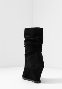 Botte compensée en daim noir avec un design effondré, un bout arrondi et une surface texturée. Dispose d'un talon compensé pour plus de hauteur.