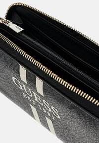 Portafoglio nero con esterno testurizzato, zip dorata e logo "GUESS" argentato con due strisce verticali. Sono visibili più scomparti.