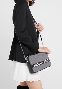 Svart och vit Michael Kors axelremsväska med geometriskt mönster, dragkedjestängning och kedjehandtag. Väskan har en rektangulär form.
