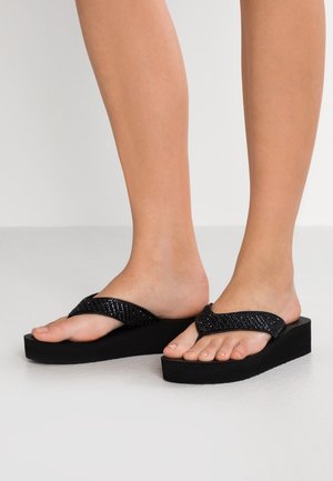 Black platform flip-flops with textured straps. The design features a wide, V-shaped toe post and a thick, matte black sole.
