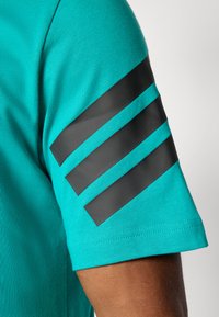 Turkisset t-shirt med sorte diagonale striber på ærmet. Fremstillet af blødt stof med en sømløs kant ved ærmet og kroppen.