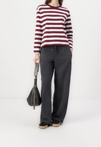 Camicia a maniche lunghe a righe bordeaux e bianche abbinata a pantaloni larghi grigi scuri. Scarpe nere e beige, piccola borsa nera con tracolla.