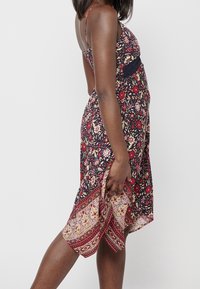 Robe d'été florale à bretelles spaghetti, fond bleu marine, motifs de fleurs rouges et roses, ourlet asymétrique et une taille texturée.