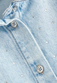 Ljusblå denimskjorta med glittrande rhinestones och silverknappar, med klassisk krage och texturerad tyg.