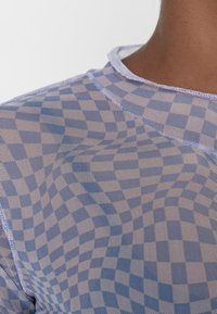 Haut en maille à carreaux bleus et blancs avec un tissu léger et transparent ; présente un col rond et une surface légèrement texturée.