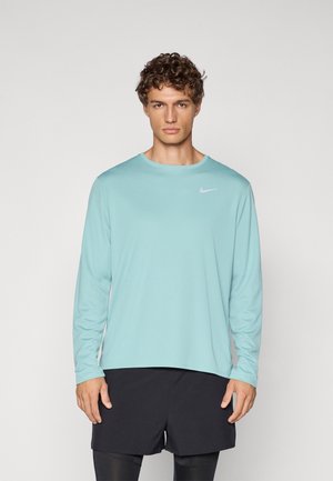 Lyseblå langærmet sportstrøje med rund halsudskæring og et lille hvidt Nike-logo på brystet, kombineret med sorte shorts.