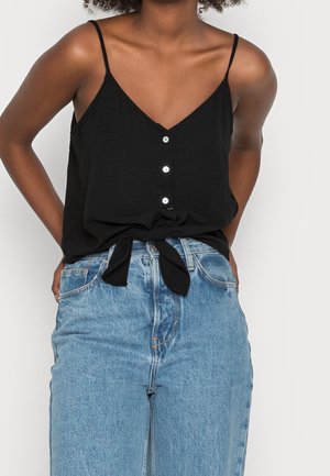 Sort ærmeløs top med V-hals og knapper foran, knyttet i taljen, kombineret med højtaljede lyseblå jeans.