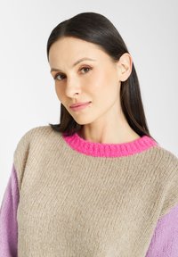 Gebreide trui met een beige lichaam, felroze geribde halslijn en lila mouwen. Zachte textuur met een comfortabele pasvorm en duidelijke kleurblokkering.