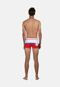 Shorts de bain rouges avec une taille élastique blanche et une petite poche sur le côté. Le design présente une coupe courte et une texture lisse.