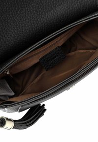 Wnętrze czarnej torebki skórzanej o fakturowanej powierzchni z brązowym wykończeniem, kieszenią na zamek i metką marki. Posiada szczegół w postaci chwosta po boku.