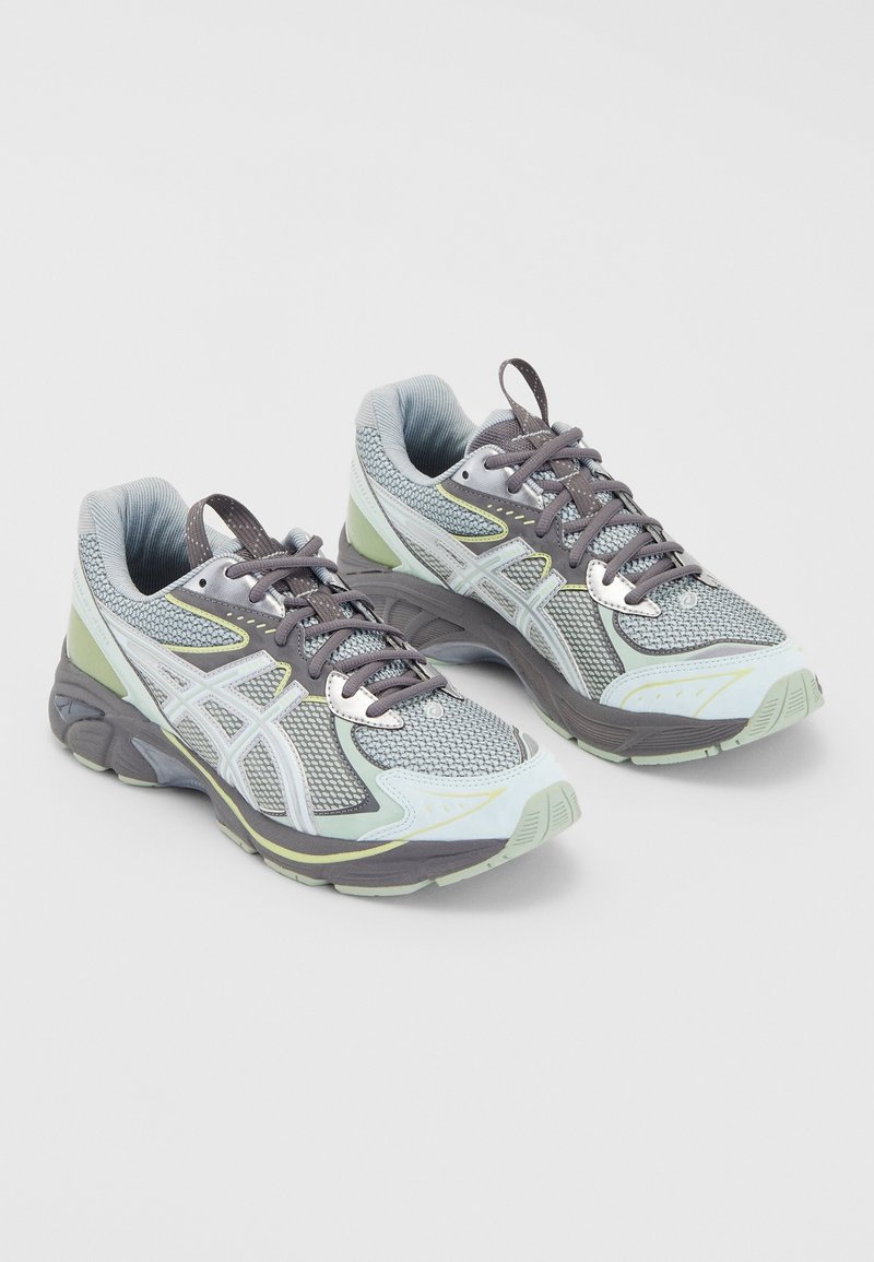 Paire de chaussures de course athlétiques grises et vert clair avec tiges en mesh, lacets et semelles épaisses et rembourrées sur fond blanc.