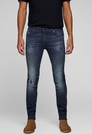 Smalfit mørkeblå jeans med en falmet tekstur, slidte detaljer, fem lommer og knaplukning, parret med brune ankelstøvler.