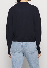Maglione lavorato a maglia blu navy con scollatura tonda e maniche lunghe, abbinato a jeans chiari a vita alta con tasche posteriori e cuciture visibili.