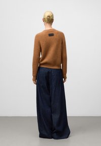 Maglione di lana marrone con colletto rotondo e un'etichetta nera sul retro, abbinato a jeans in denim scuro a gamba larga. Tessuto a maglia testurizzato.