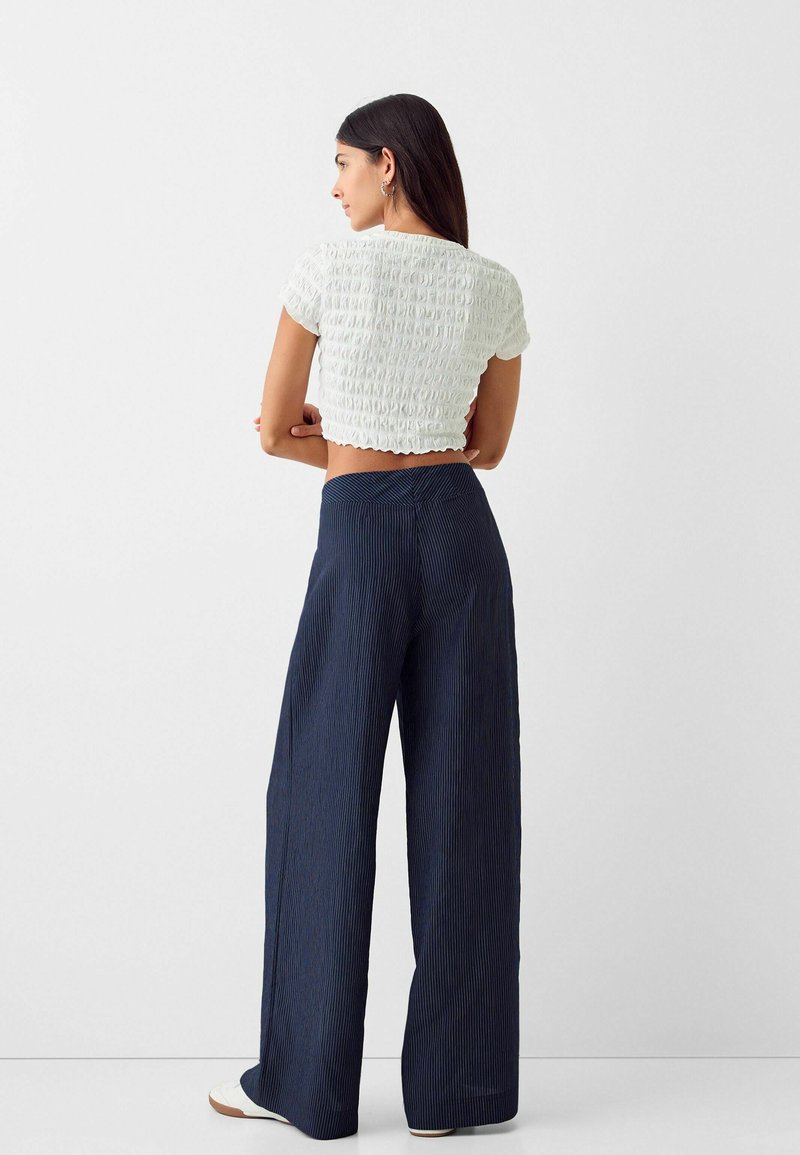 Top corto bianco con motivo testurizzato e maniche corte, abbinato a pantaloni a gamba larga a righe blu navy. L'outfit ha una vestibilità comoda.