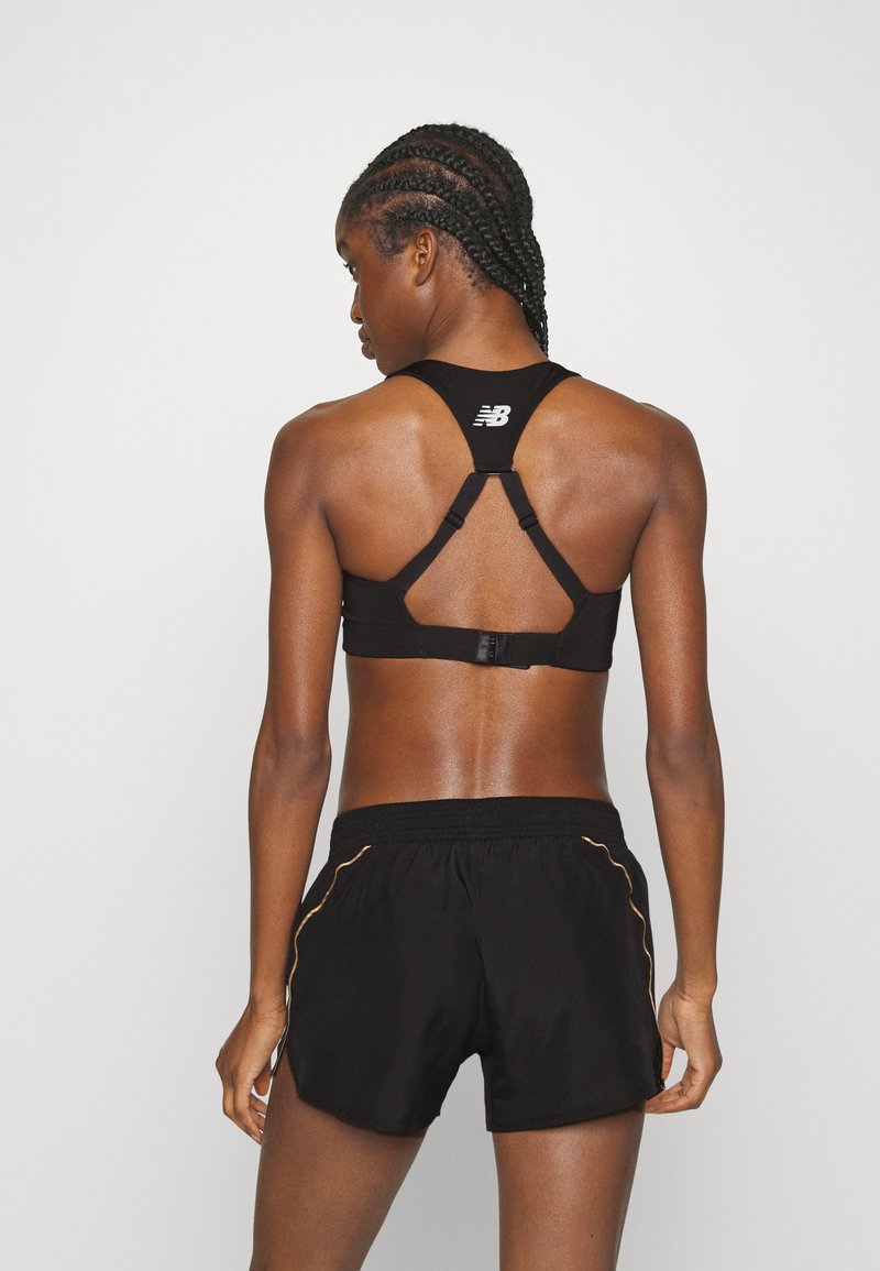 Sujetador deportivo negro con diseño de espalda nadadora y tirantes ajustables, combinado con pantalones cortos negros con detalles dorados a lo largo de las costuras laterales.