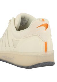 Cremefarvet sneaker med tekstureret overdel, orange detaljer og en gennemsigtig sål. Har en polstret krave og et mærke indeni.