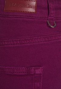 Tejido de mezclilla en fucsia con una etiqueta de cuero que presenta un logo en relieve. Incluye costuras detalladas y un acento de bucle metálico en la cinturilla.