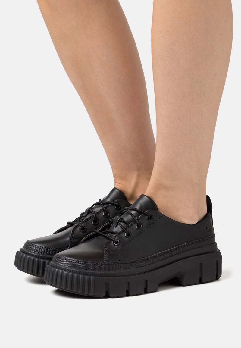 Baskets en cuir noir avec une semelle en caoutchouc épaisse, un bout rond et un design à lacets. Elles présentent des détails de couture et un logo subtil sur le talon.