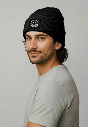 Black ribbed beanie with a logo patch featuring waves and mountains, worn by a person in a light gray shirt, showing textured fabric details.