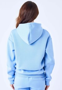 Sweat à capuche bleu clair avec capuche à cordon, poignets et ourlet côtelés. Texture lisse et coupe décontractée, conçu pour le confort.