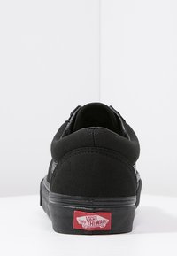 Sneaker nera in tela con design a bassa altezza, suola piatta e logo rosso "Off the Wall" sul tallone. Presenta cuciture rinforzate e una superficie testurizzata.