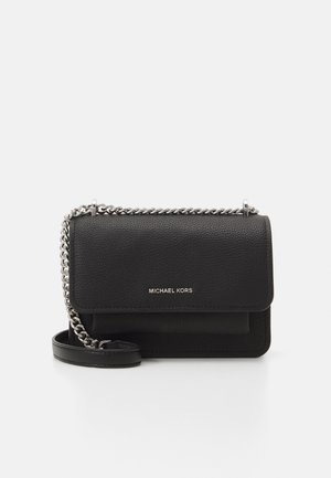 Sac bandoulière Michael Kors en cuir noir avec une sangle en chaîne argentée et un logo sur le rabat avant sur fond blanc.