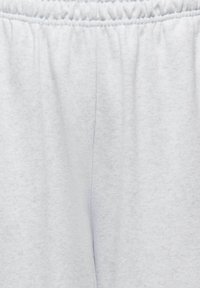 Gros plan sur un tissu gris clair avec une taille élastique et une couture centrale, probablement une partie de vêtements décontractés comme un pantalon de survêtement ou un short.