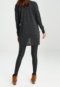 Lång, mörkgrå tröja i stickad tyg, med avslappnad passform, sidofickor och rundad nederkant. Matchas med svarta leggings och bruna ankellånga stövlar.